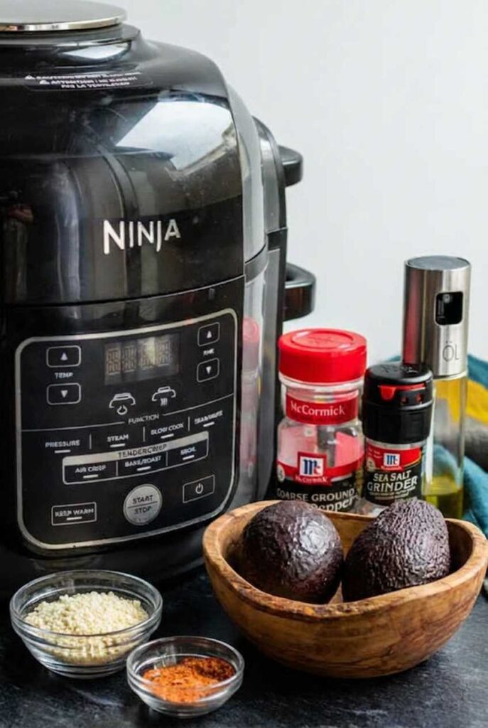 Ingredients including whole avocados, breadcrumbs, and spices next to a Ninja Air Fryer.